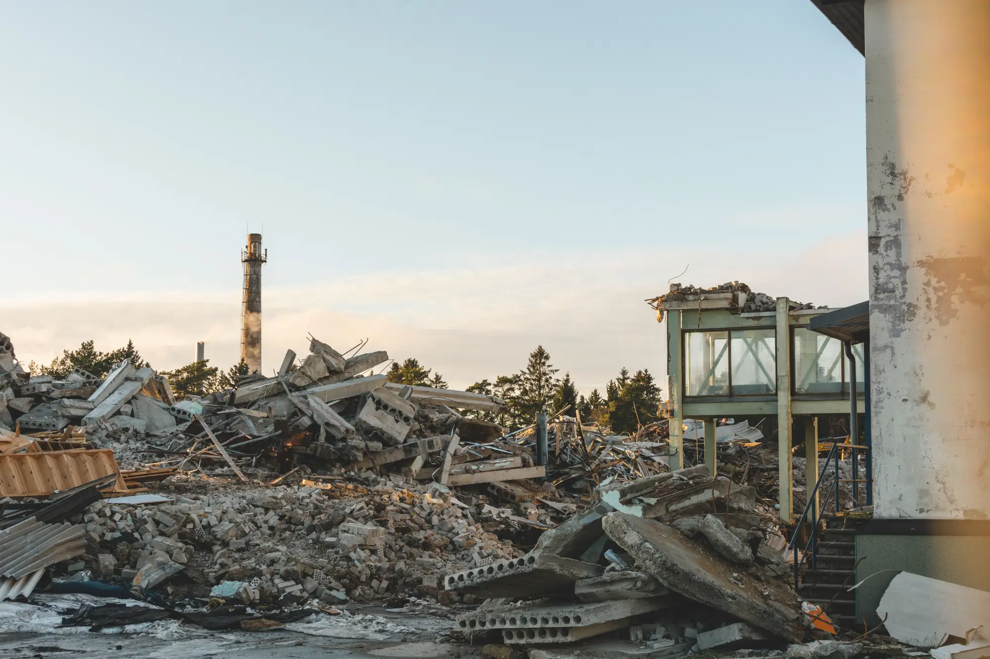 Concrete rubble on a demolition site, a tall chimney behind it under a pale sky